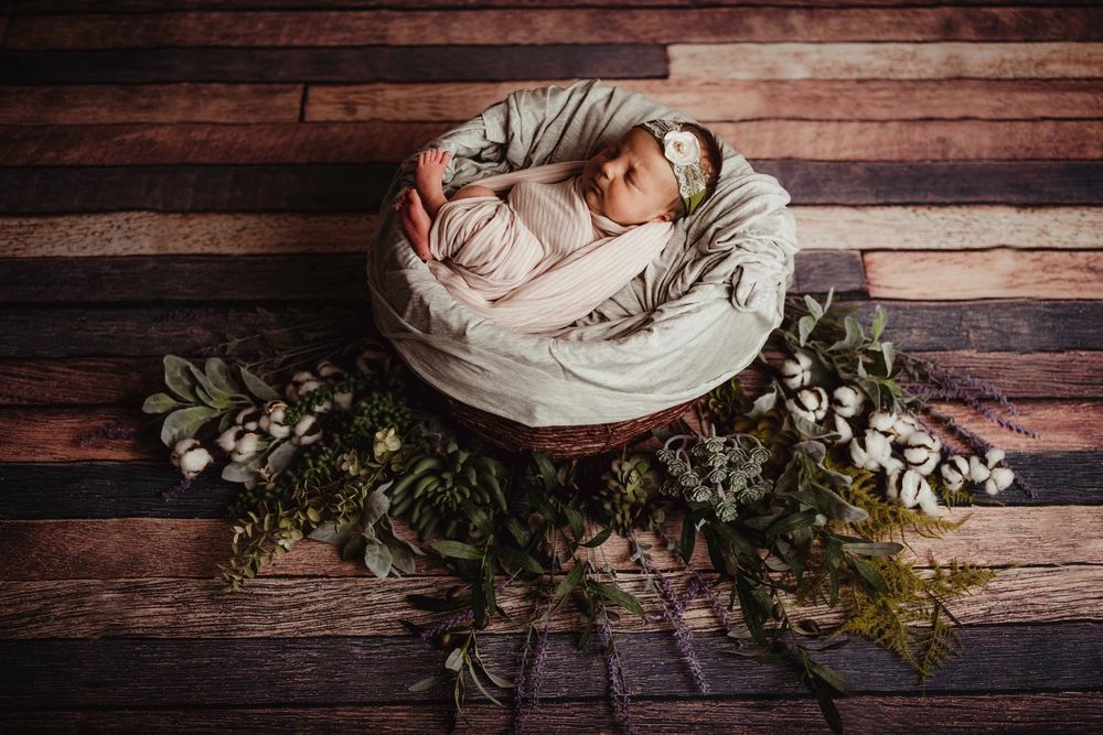 Newborn photography setup with rustic wooden backdrop and delicate floral arrangements.
