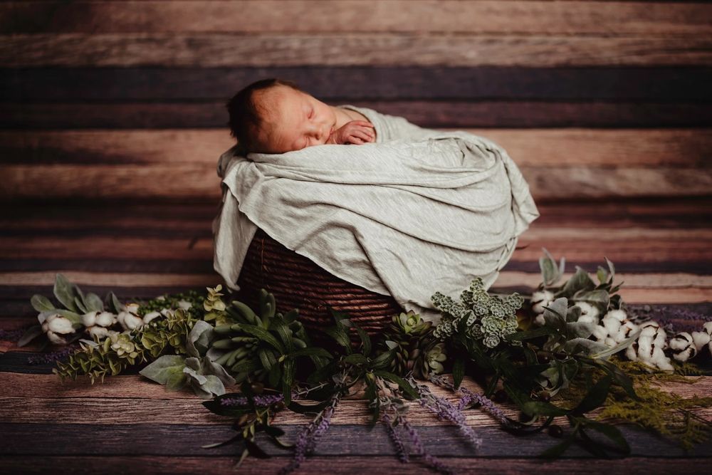 Artistic newborn photography with rustic wooden backdrop and greenery accents.