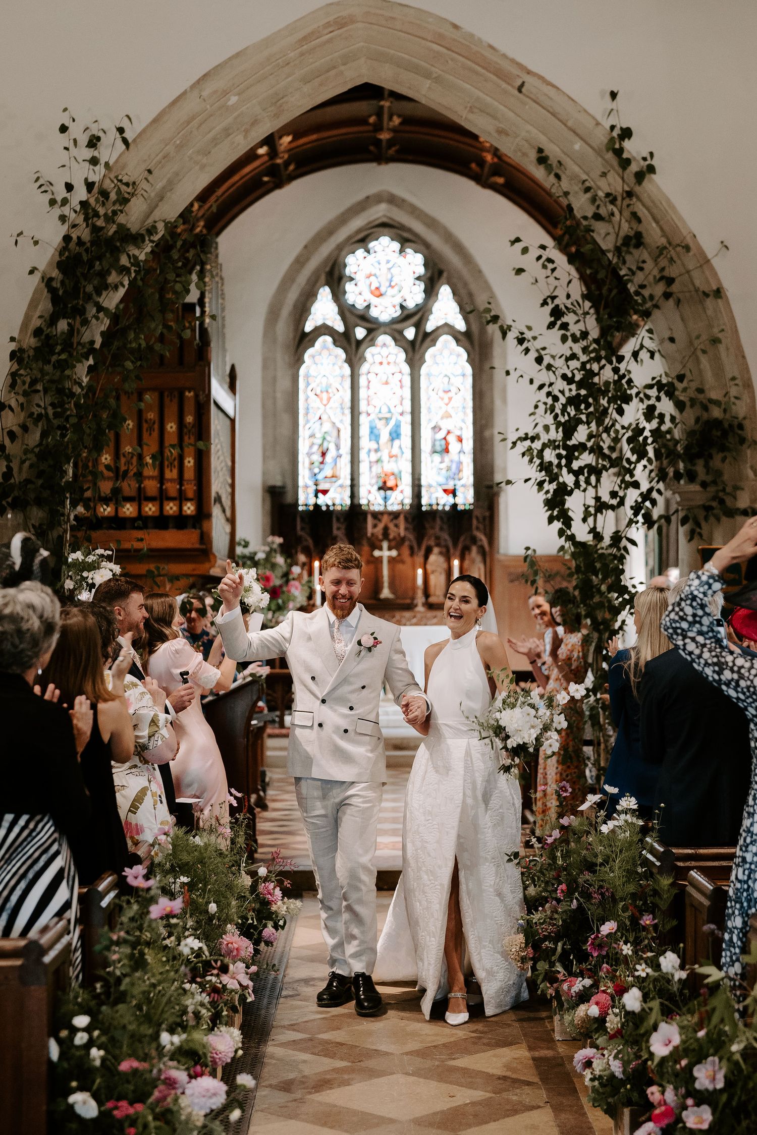 bride and groom cheering as they exit the church surrounded by their wedding guests at st Nicholas church in Oxfordshire