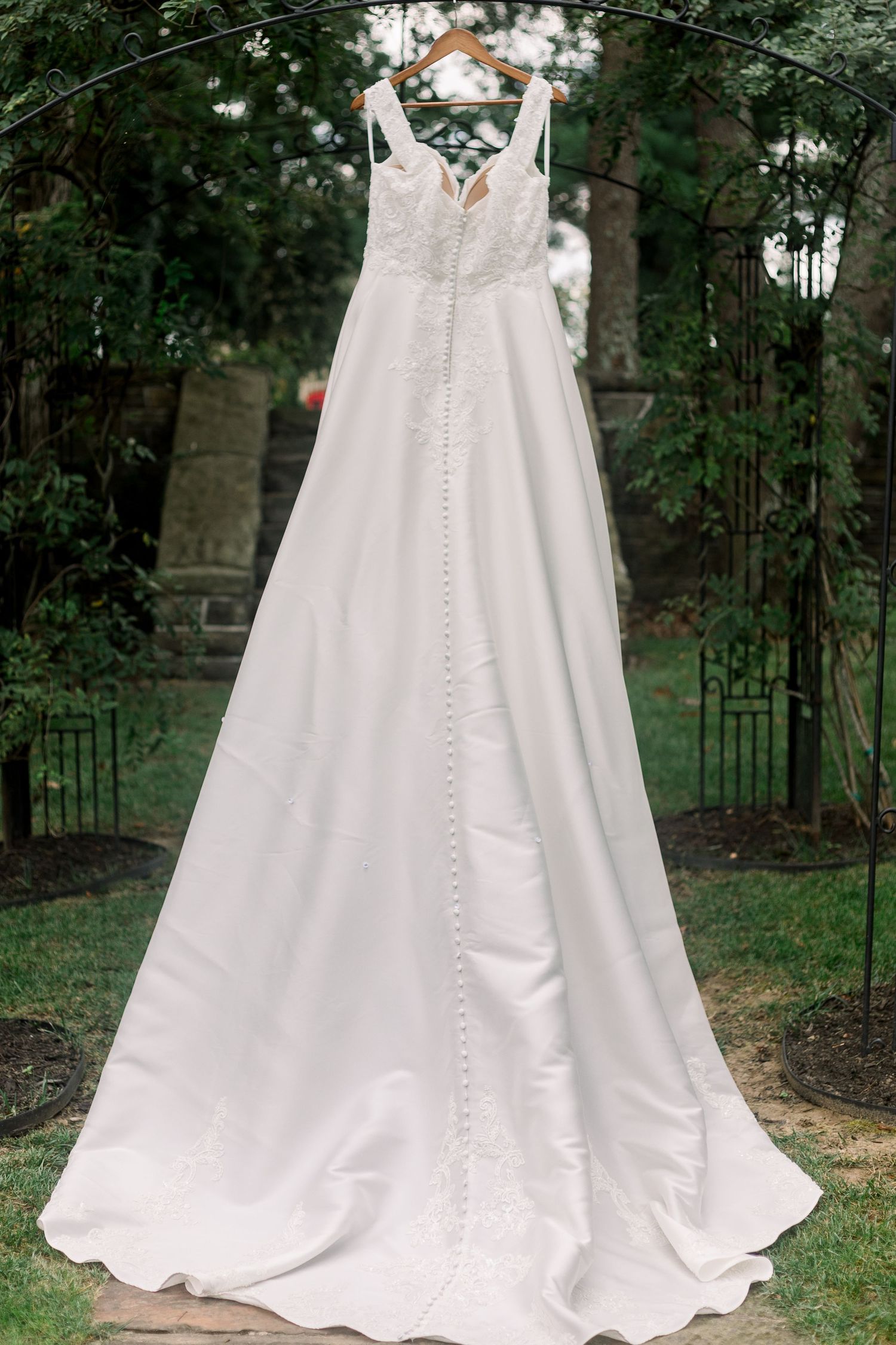 Elegant white satin wedding gown displayed in an outdoor garden setting.