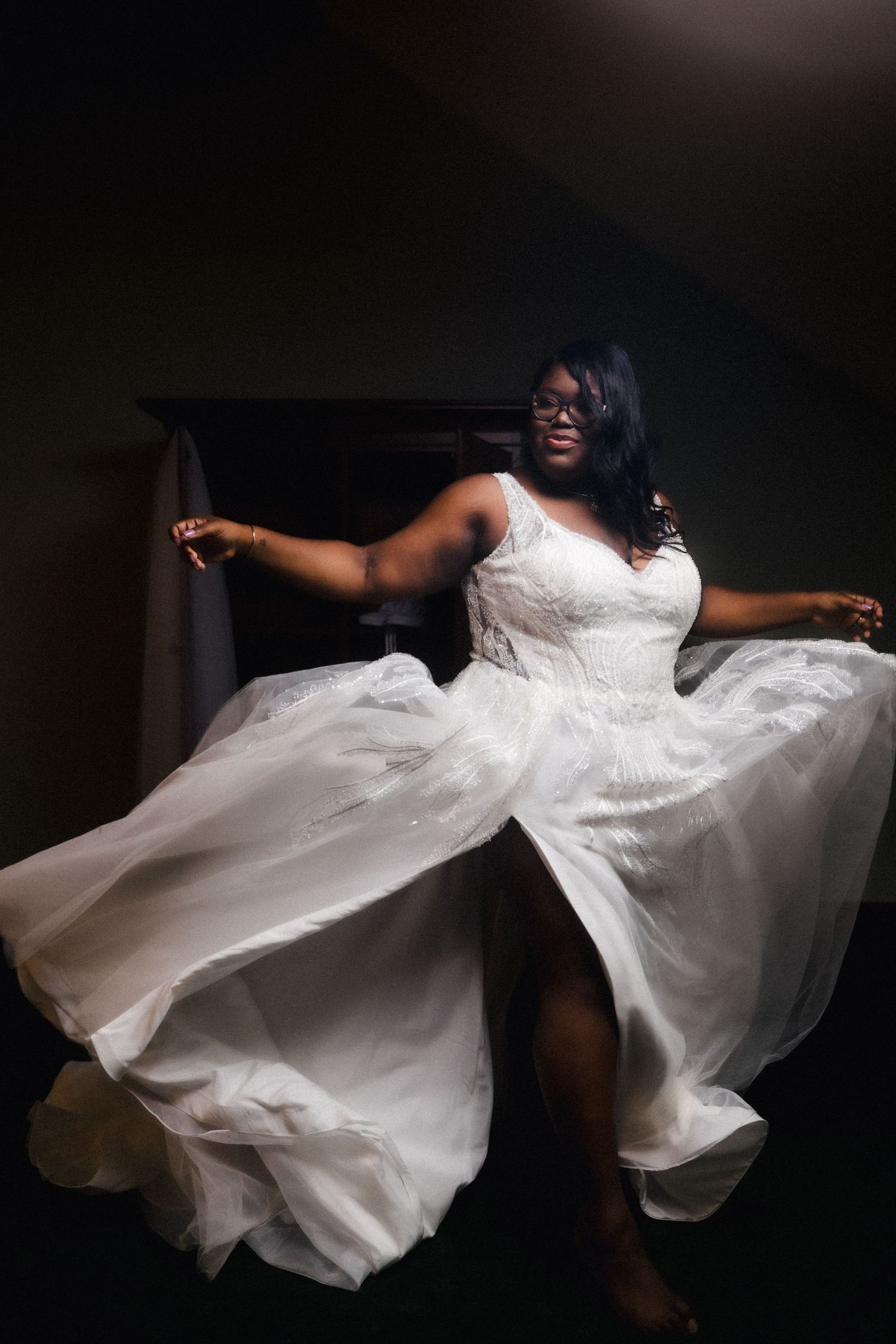 Bride in a flowing white dress twirling in dramatic lighting.