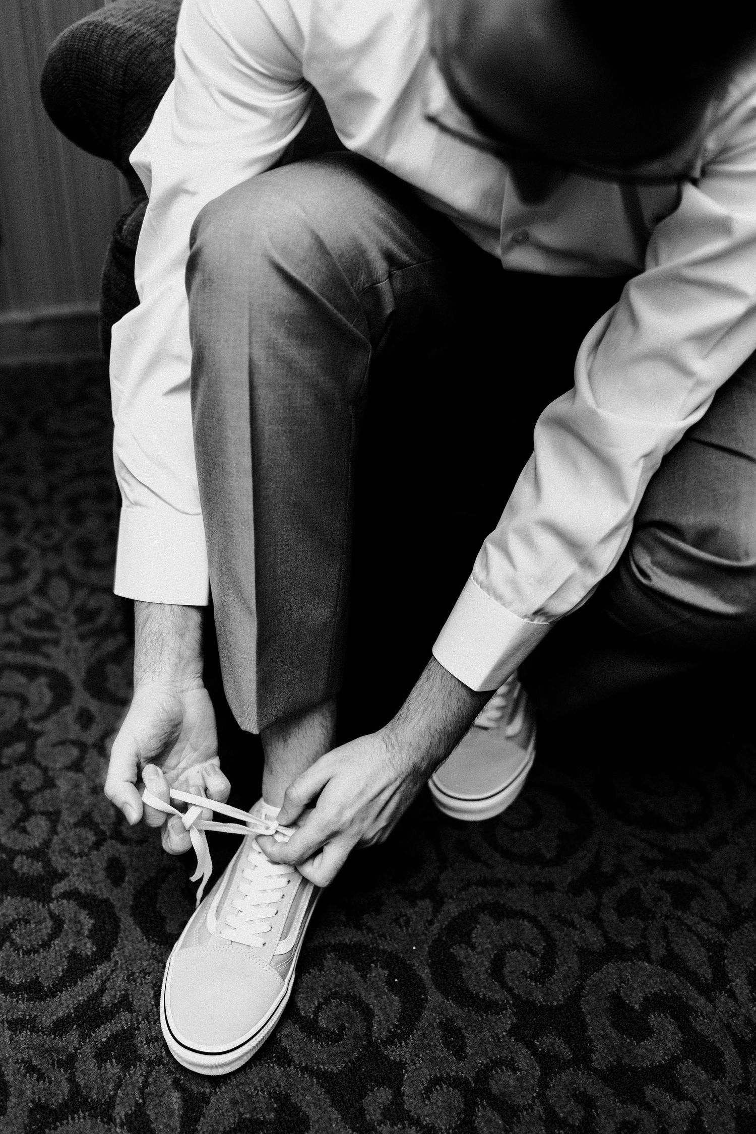 A black and white photo of someone tying white sneakers on patterned carpet.