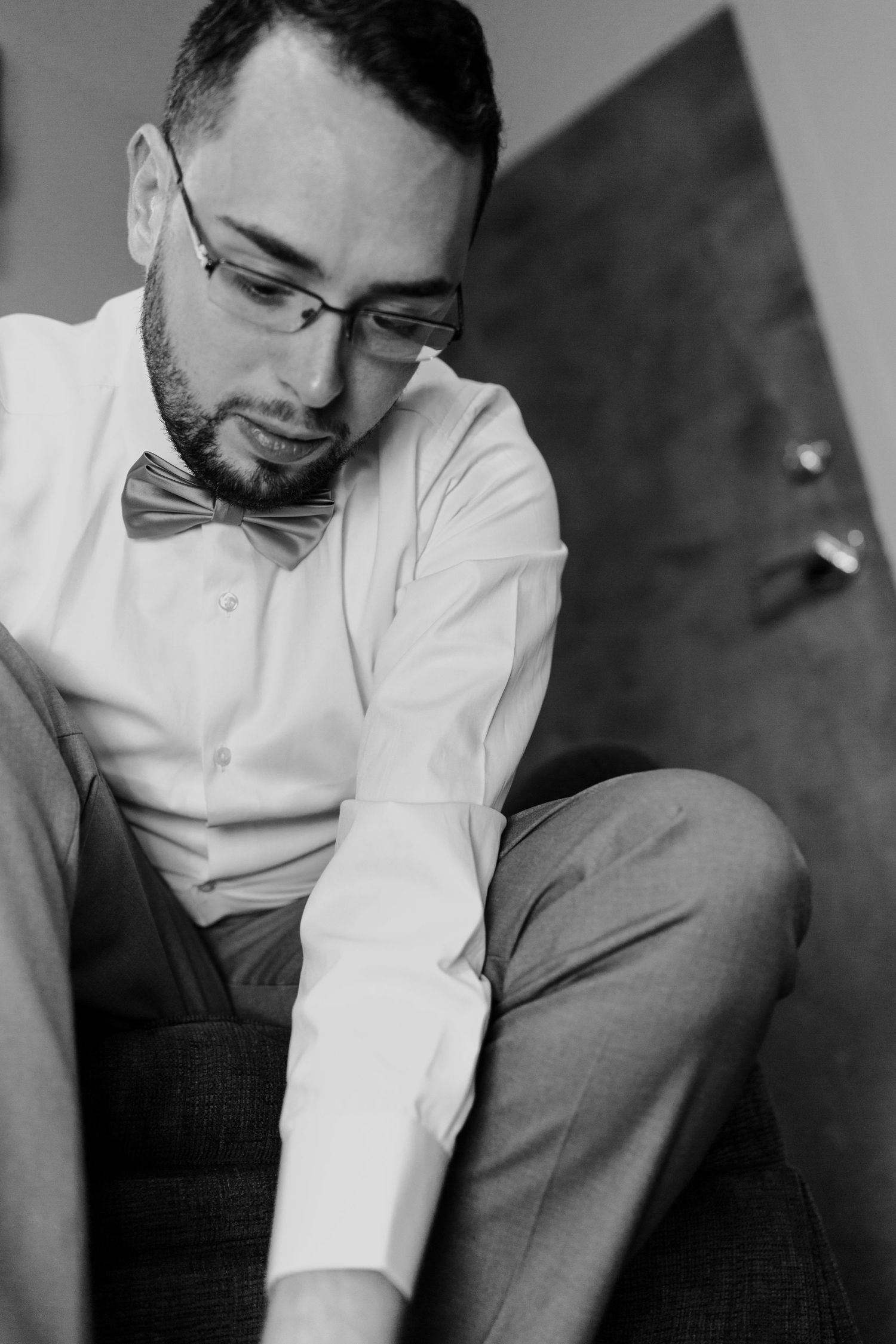 A black and white portrait of someone wearing a bowtie and glasses looking downward.
