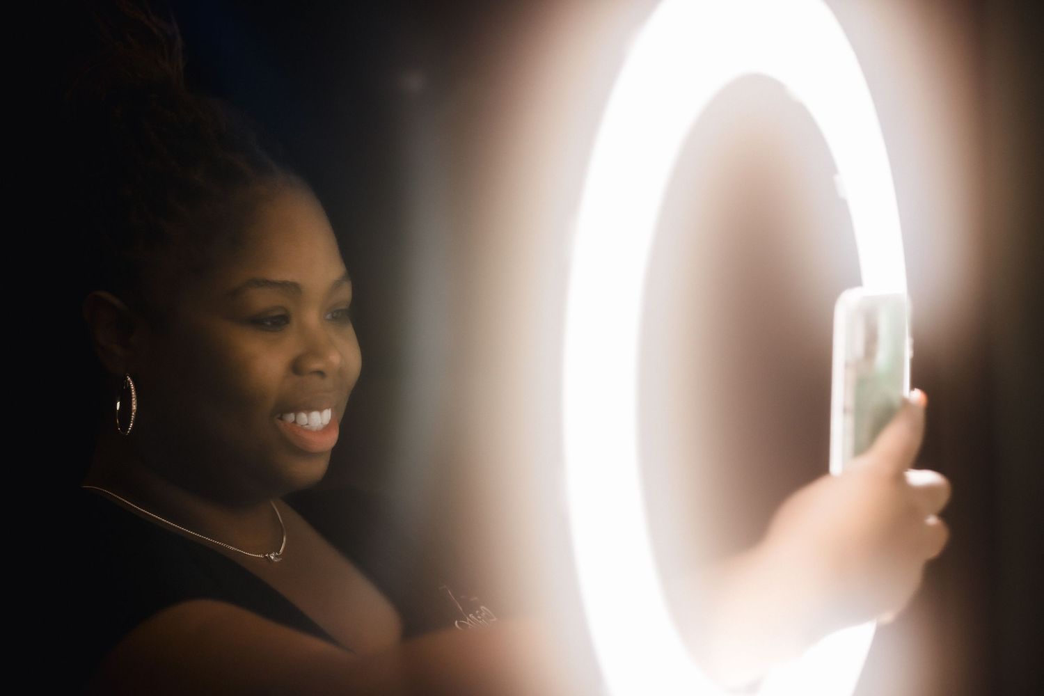 A glowing ring light reflects in frame while someone smiles during a photo session.