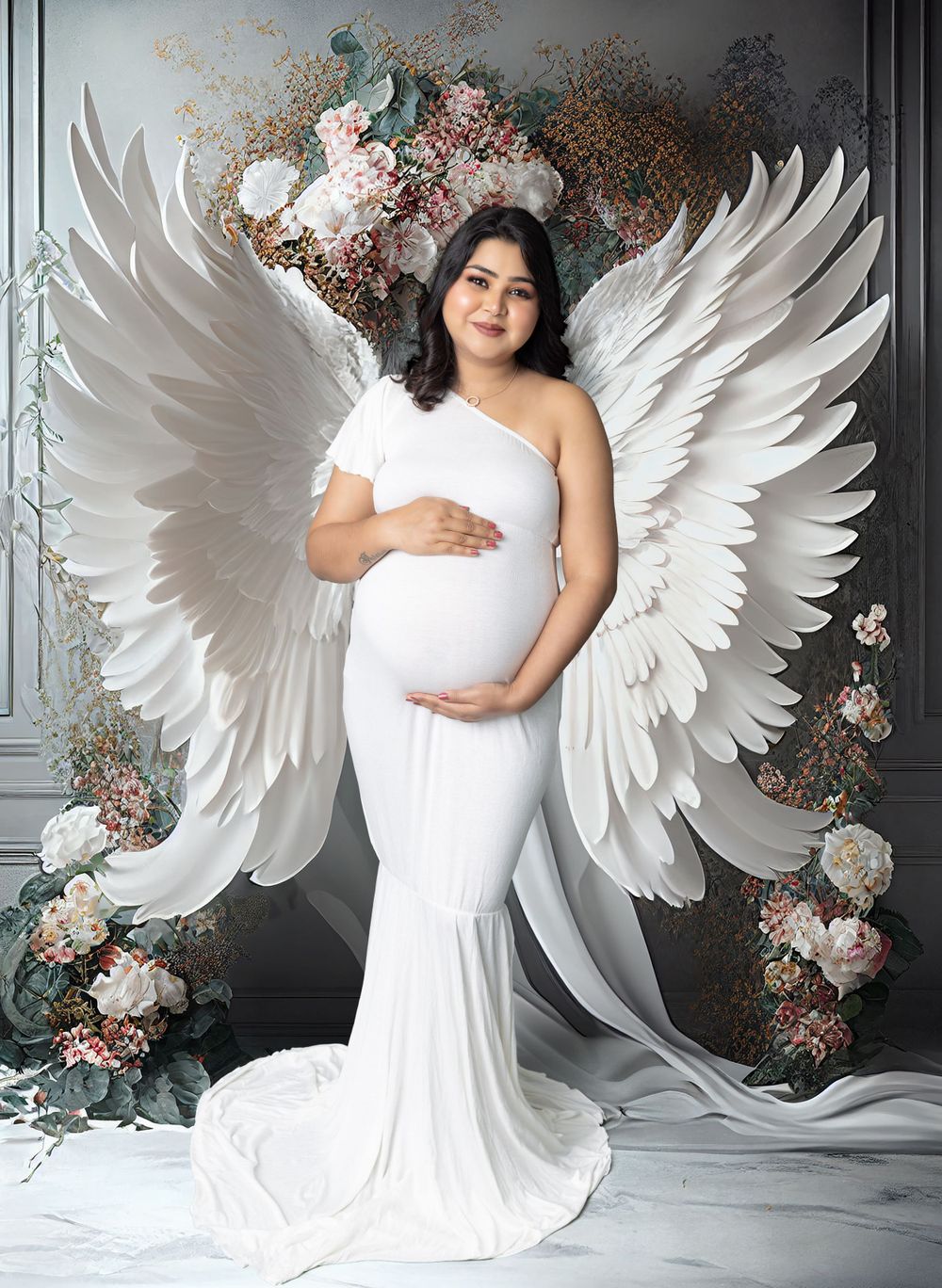 Angelic maternity portrait with white wings and floral arch backdrop.