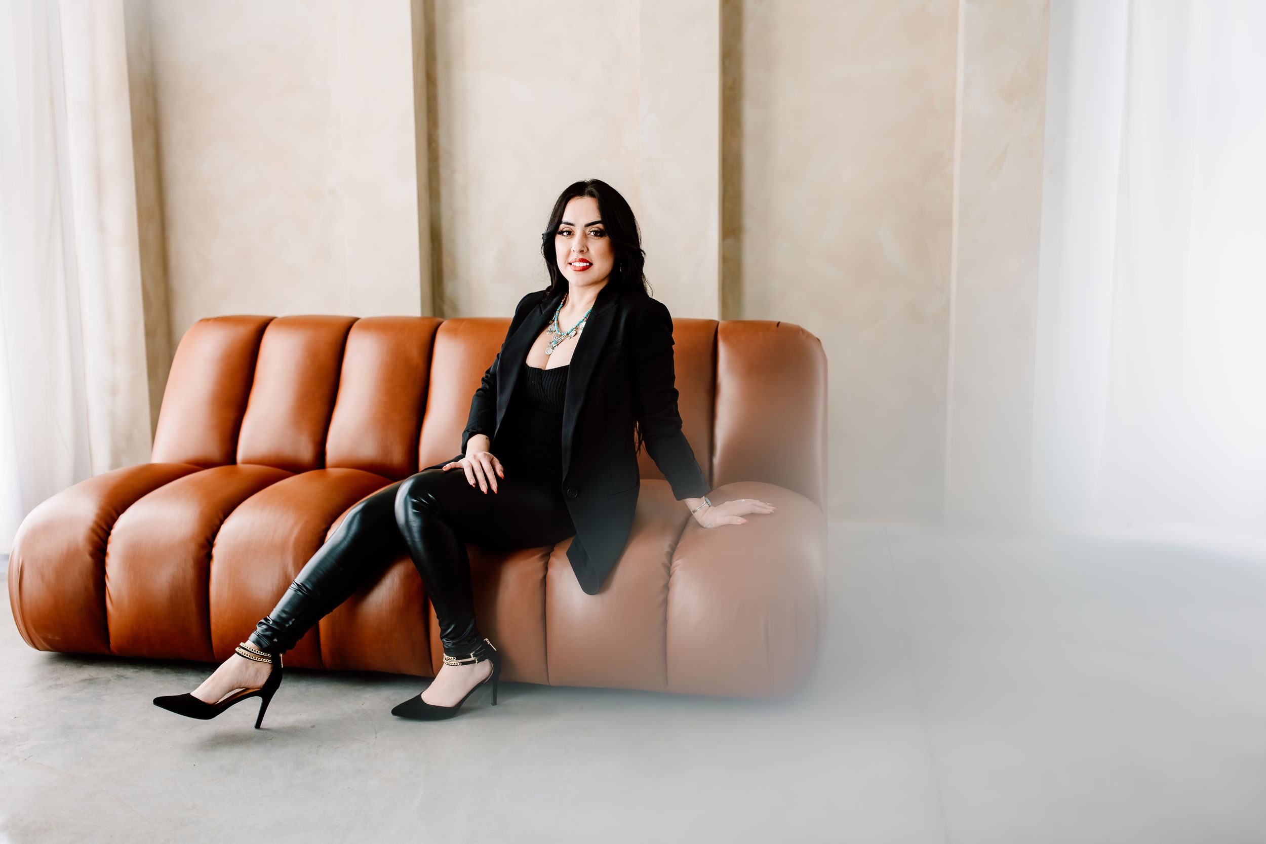 Modern studio portrait on tan leather sofa wearing black business attire.