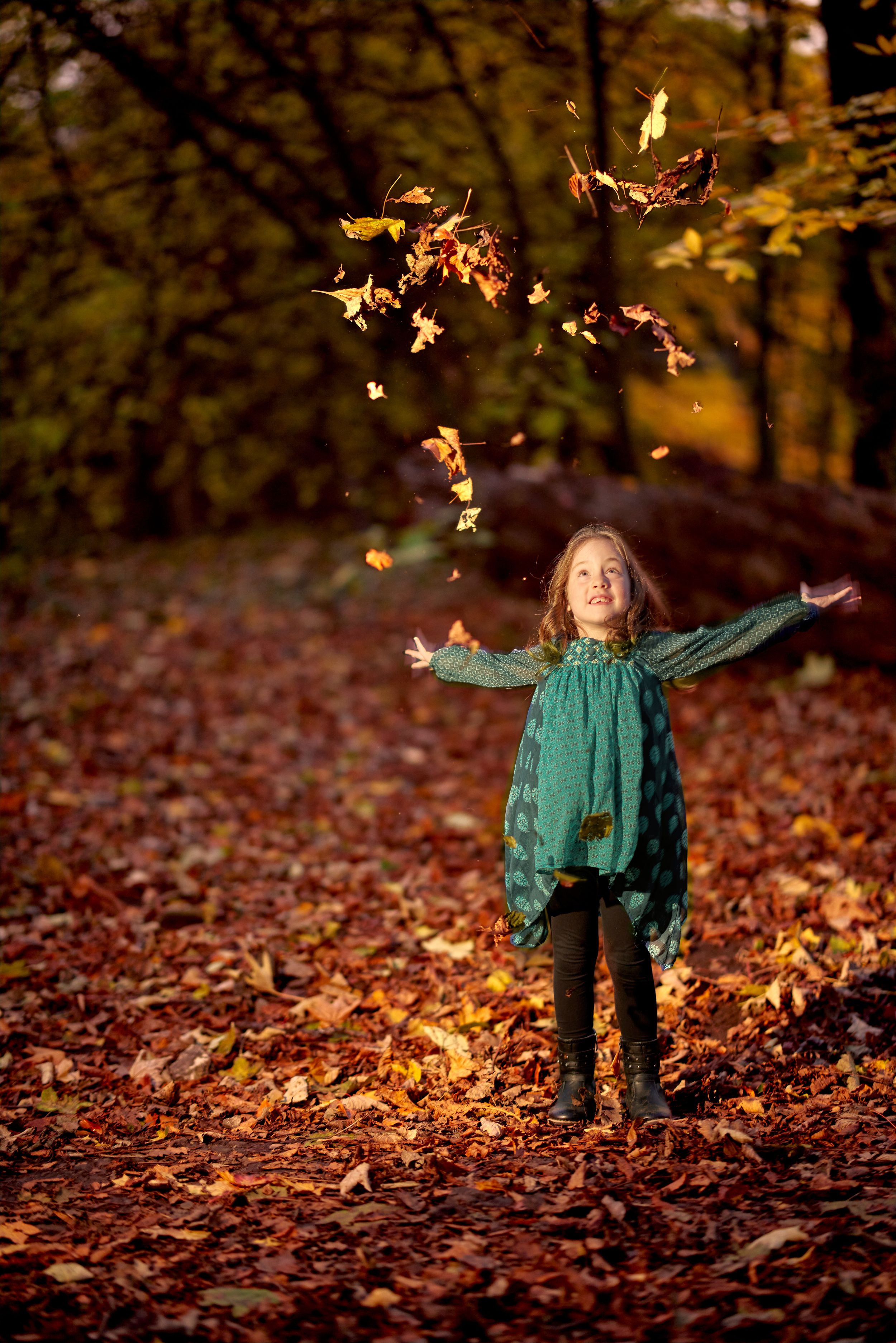 Portrait of a girl in the woods playing with autumn leaves.