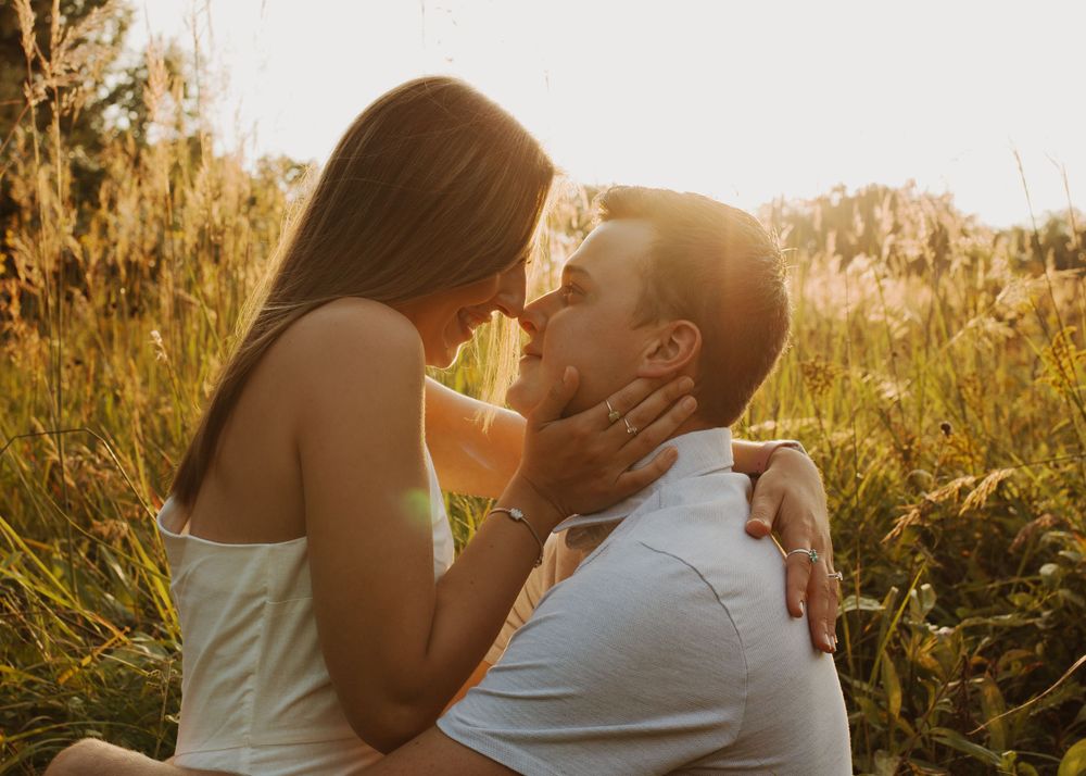 Romantic couple embraces in tall grass during golden hour sunset.