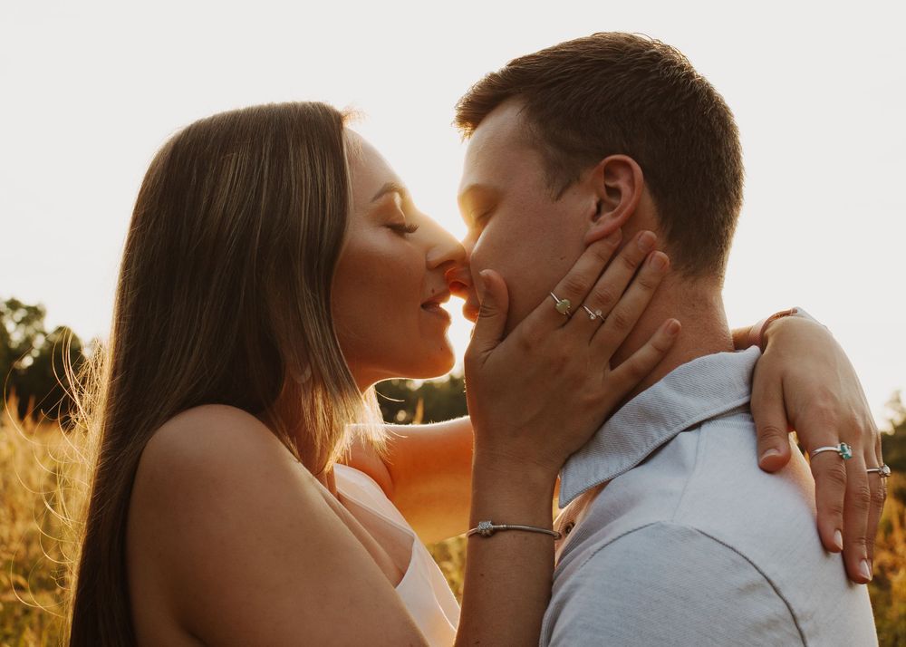 Couple sharing tender kiss in golden evening light surrounded by tall grass.