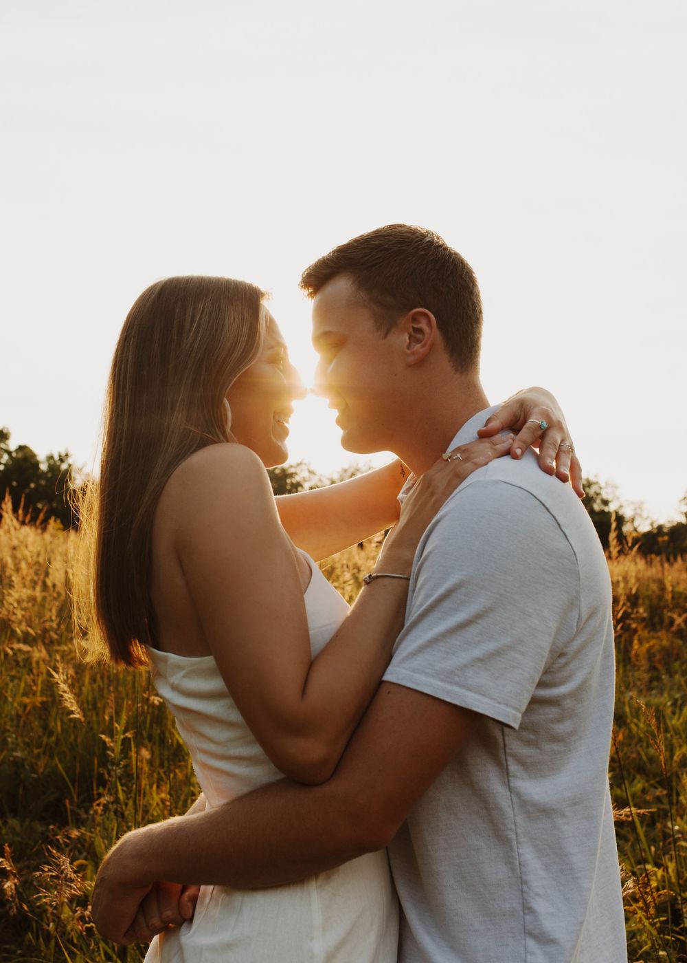 Couple embracing in warm sunset light with backlit golden glow through grass.