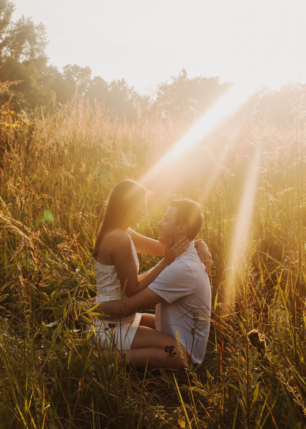 Couple shares tender moment in sunlit meadow during golden hour.