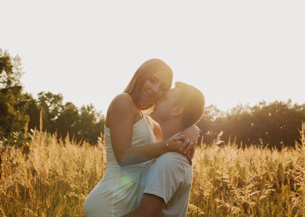 Couple embraces while bathed in warm sunset light among tall grass.