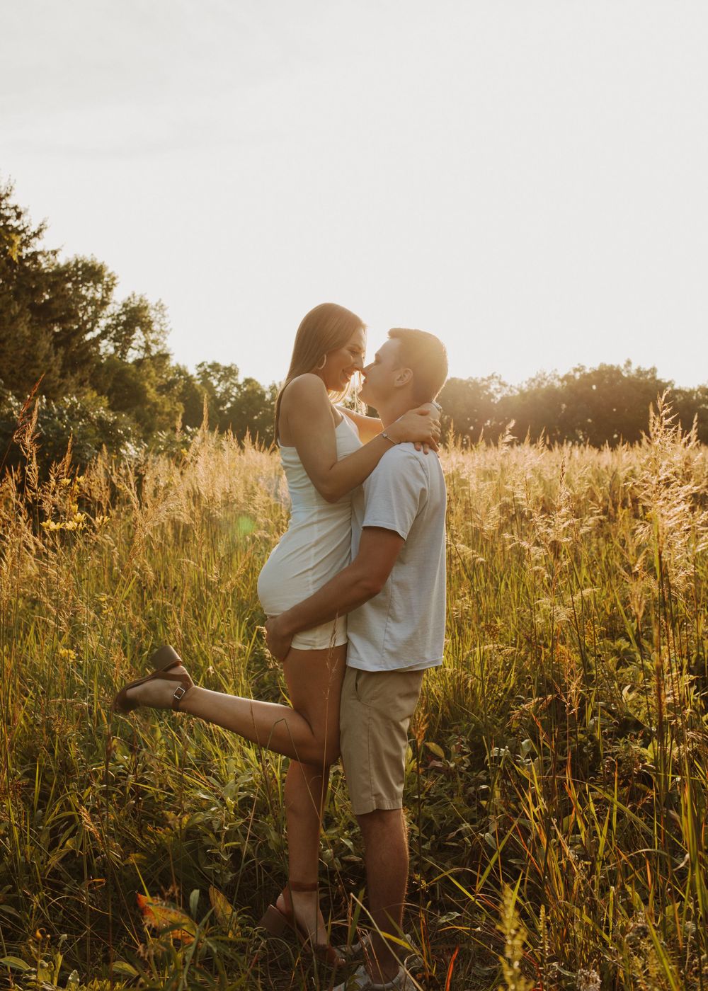 Romantic couple posing in sunset meadow with golden backlighting.