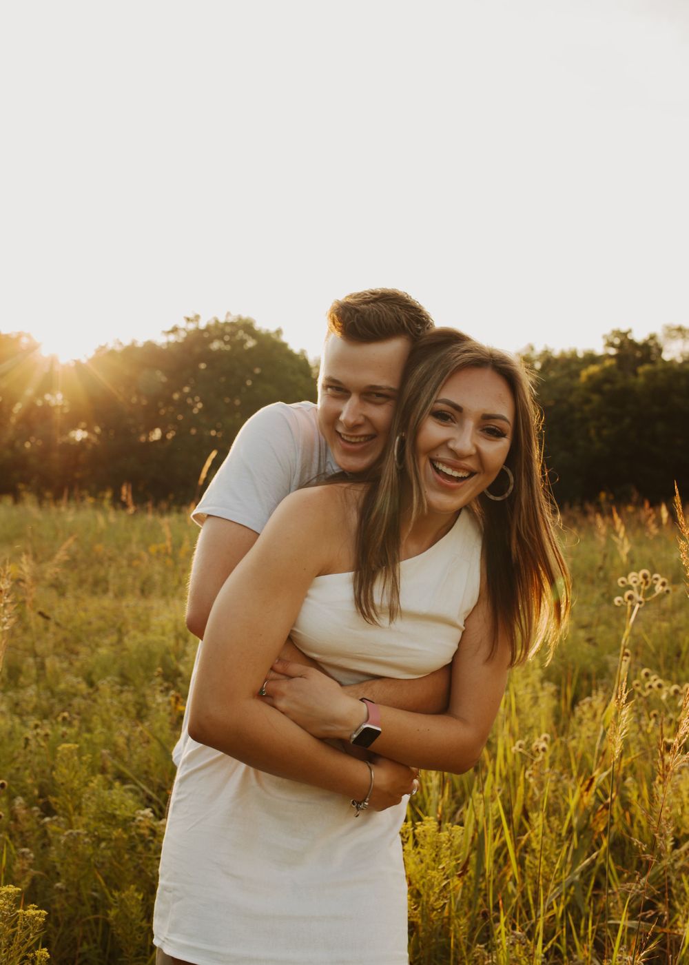Happy couple shares joyful embrace in golden field at sunset.