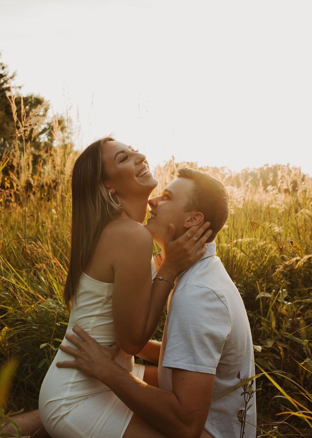 Intimate couple shares laughter while embracing in a sunlit field of tall grass.