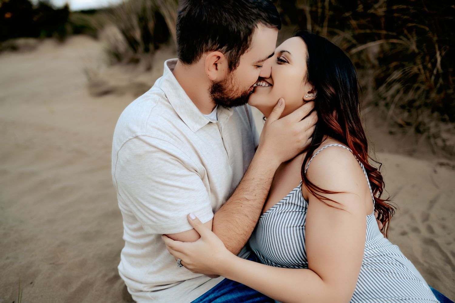 Romantic couple embracing on sandy beach dunes during sunset photoshoot.