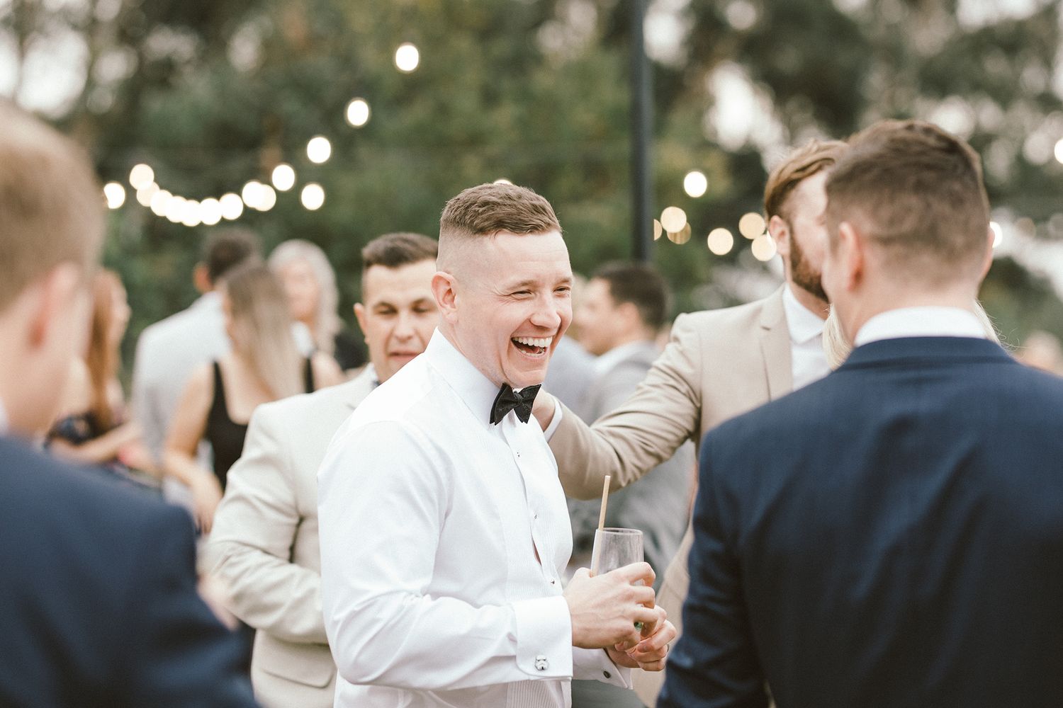 Wedding guest laughing during outdoor cocktail reception with string lights.