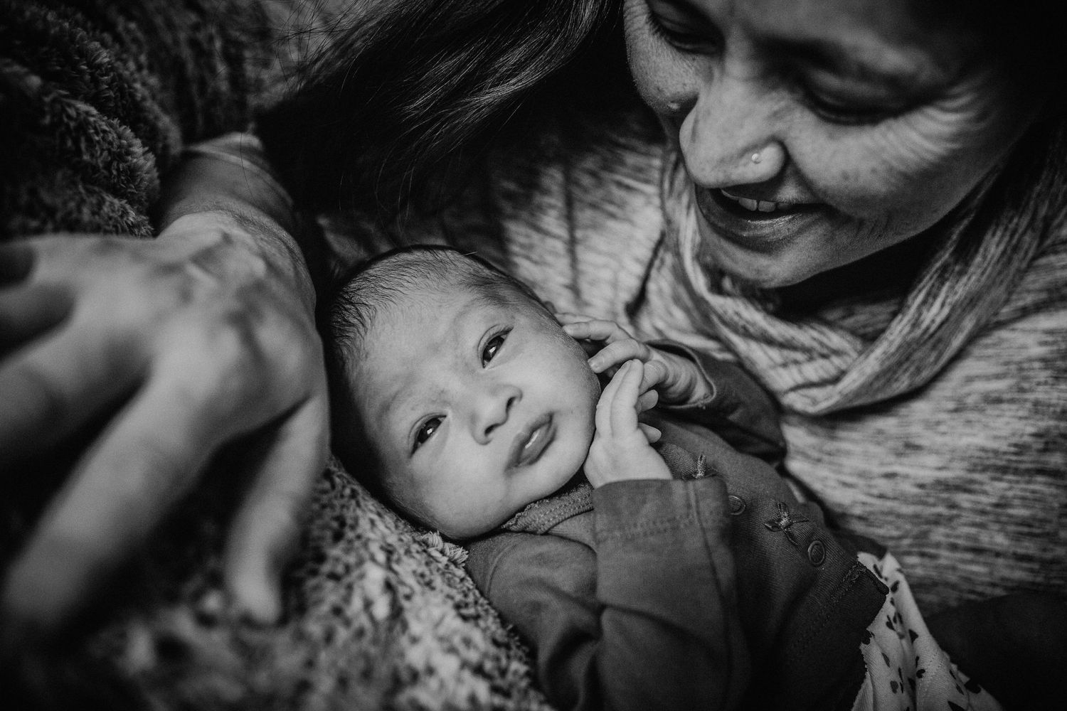 Candid black-and-white portrait of Asian mother with her newborn baby. Mom smiles at Baby while Baby touches her face.