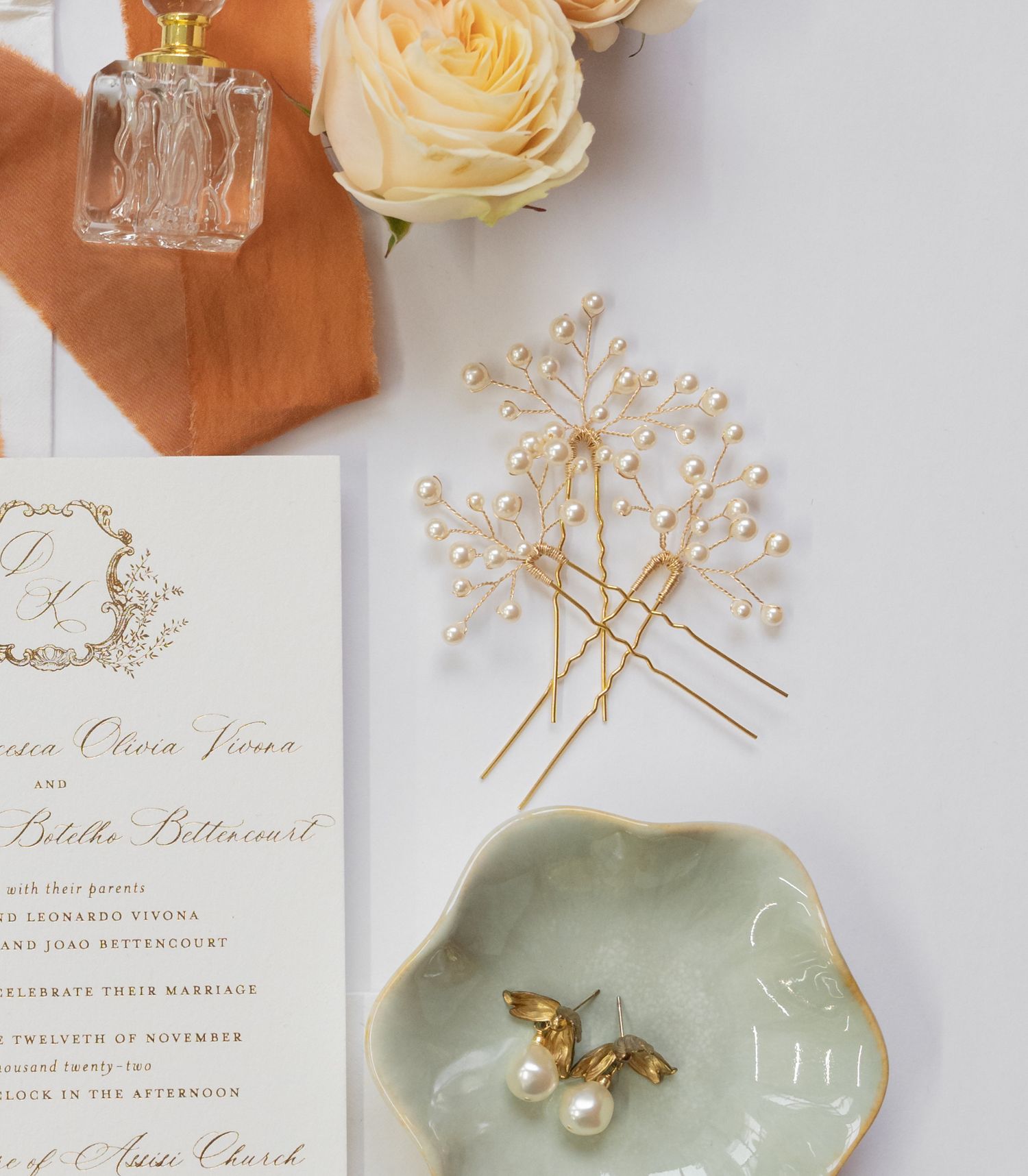 Wedding details flatlay with pearl hairpins, floral invitation, and delicate jewelry on a ceramic dish.