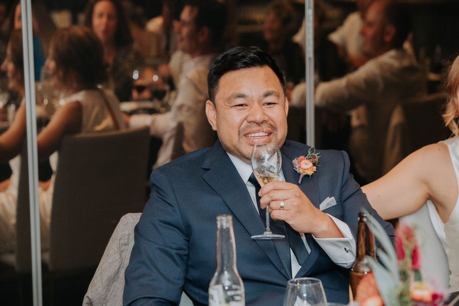Guest in navy suit gives speech at wedding reception with drinks on table.