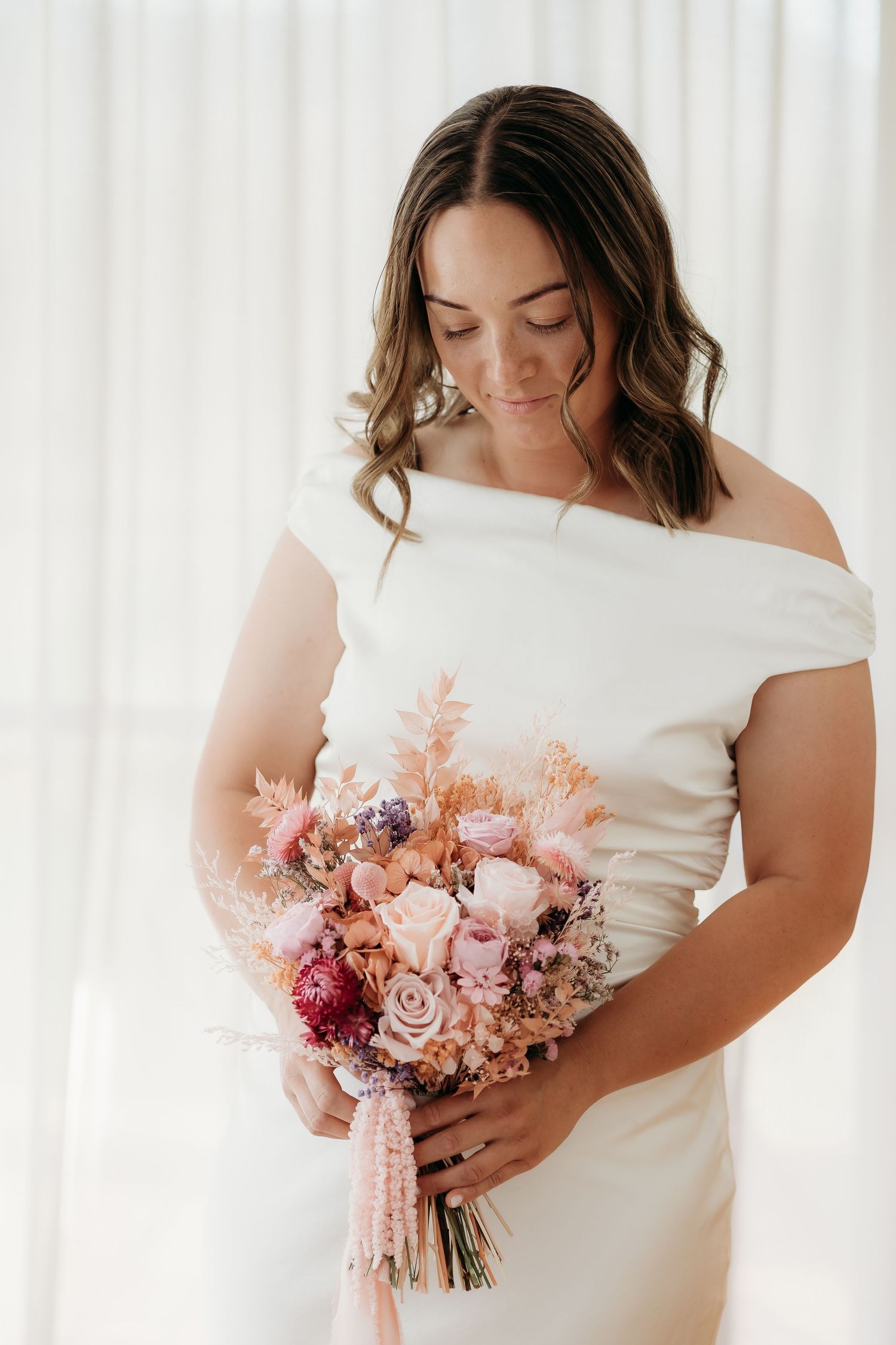 Close-up of pink and burgundy bridal bouquet with roses against white fabric.