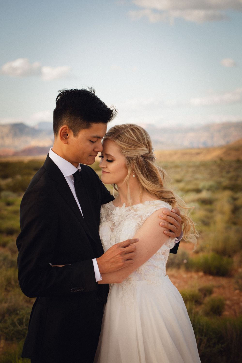 Bride and groom share an intimate forehead touch in a desert landscape with mountains in the background.