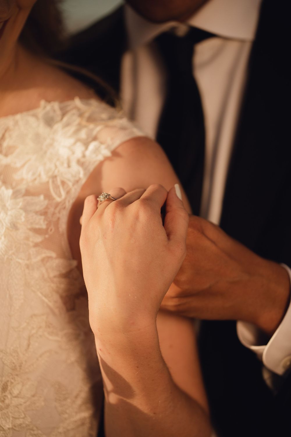 Close-up of bride and groom holding hands revealing a sparkling diamond engagement ring.