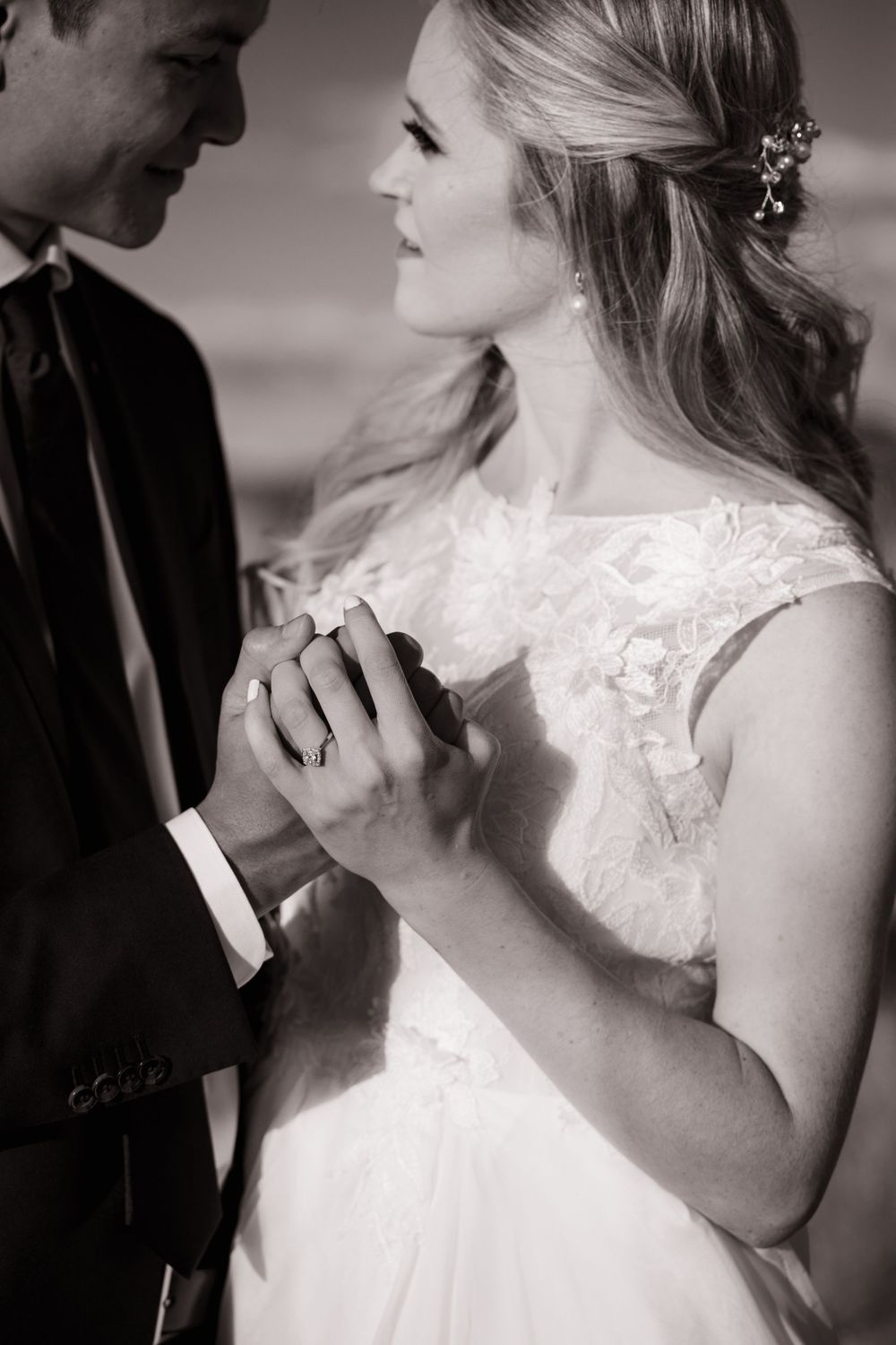 Black and white portrait of bride and groom holding hands, bride wearing lace gown and hair accessory.