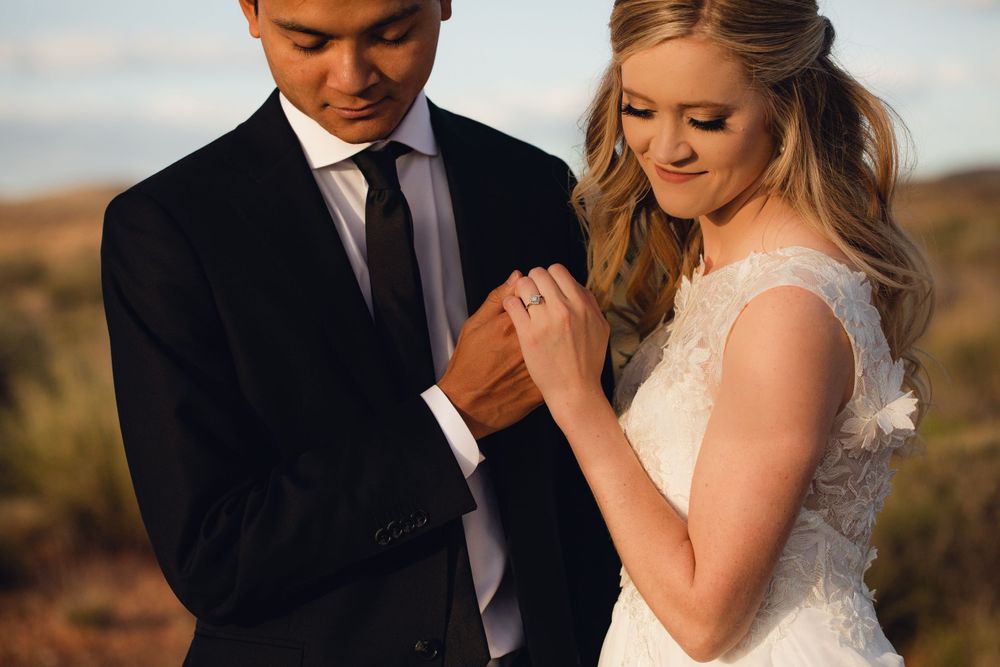 Close-up of groom holding bride's hand admiring wedding ring in warm desert setting.