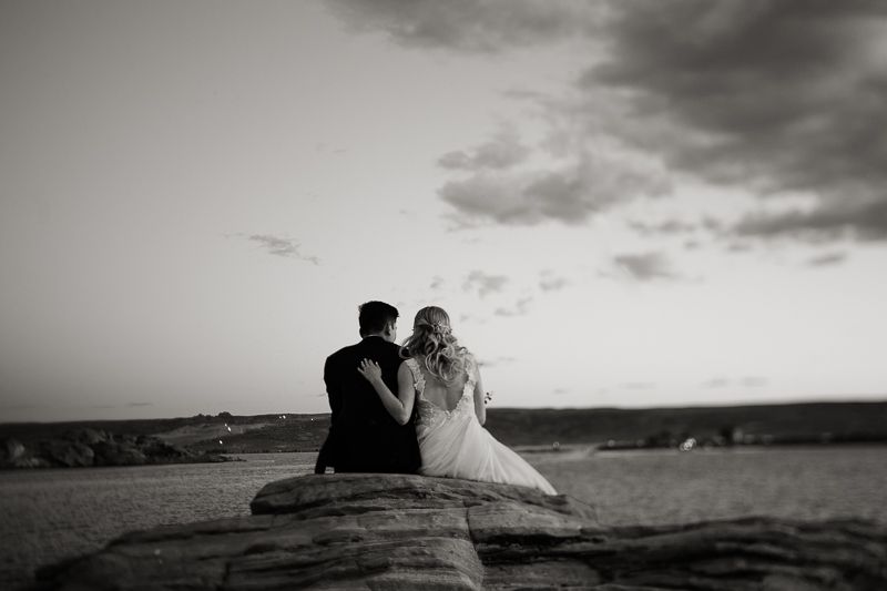Black and white photo of bride and groom sitting close together on rocky landscape.