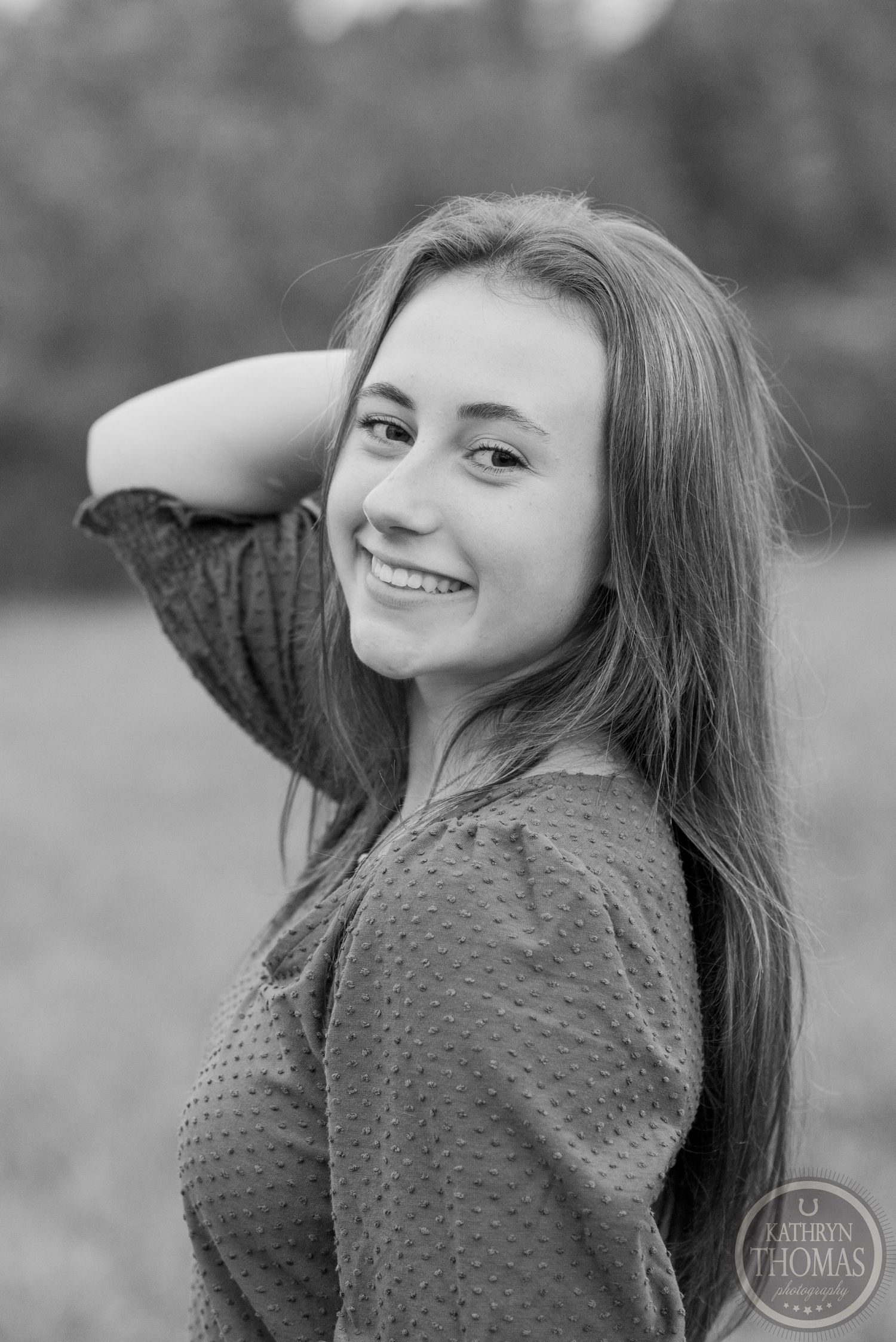 Black and white portrait of someone with long hair wearing a textured sweater outdoors.