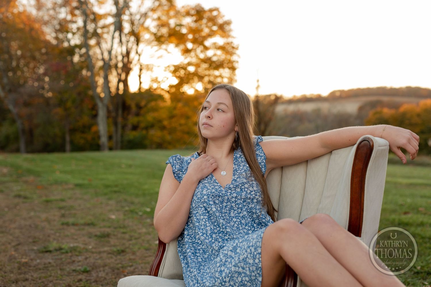 Person relaxes in vintage armchair outdoors during autumn sunset wearing blue floral dress.