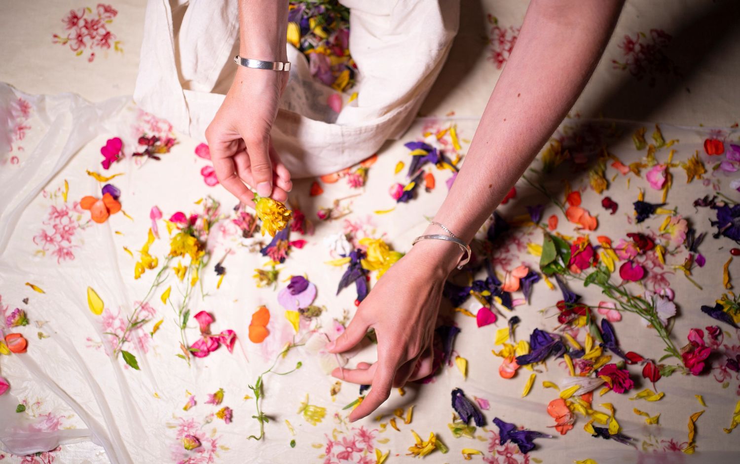 a table covered with fabric and petals and flower, with two hands arranging