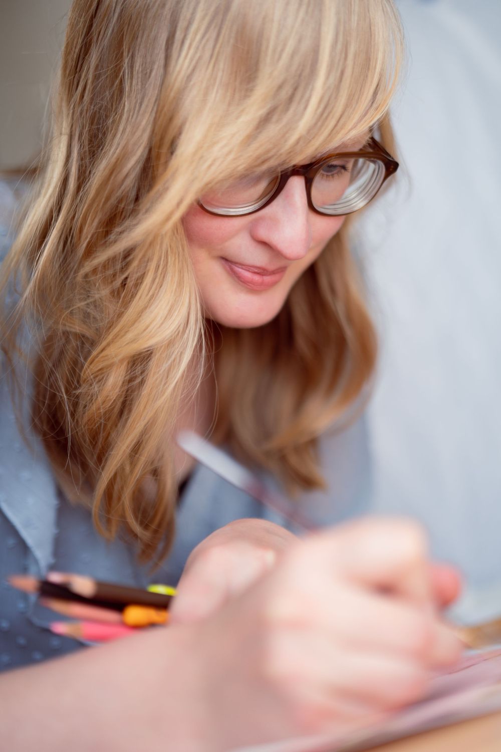 Anna Sikkes en haar karakteristieke uiterlijk omlijst met losse haren gefotografeerd terwijl ze met handen vol potloden illustreert