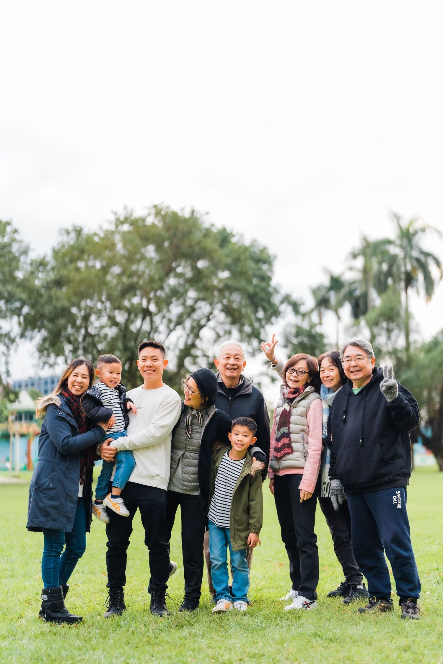Extended family posing together on grass with palm trees in background.