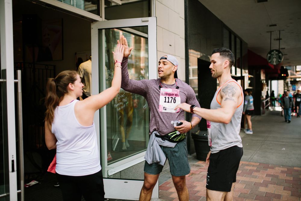 Three people high-five outside a storefront, with one wearing race bib number 1176 during a running event.