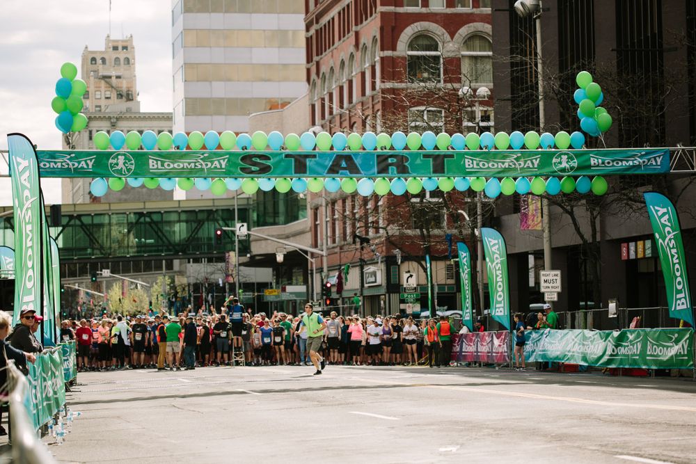 Runners gather at green balloon arch start line of Bloomsday road race in downtown city street.