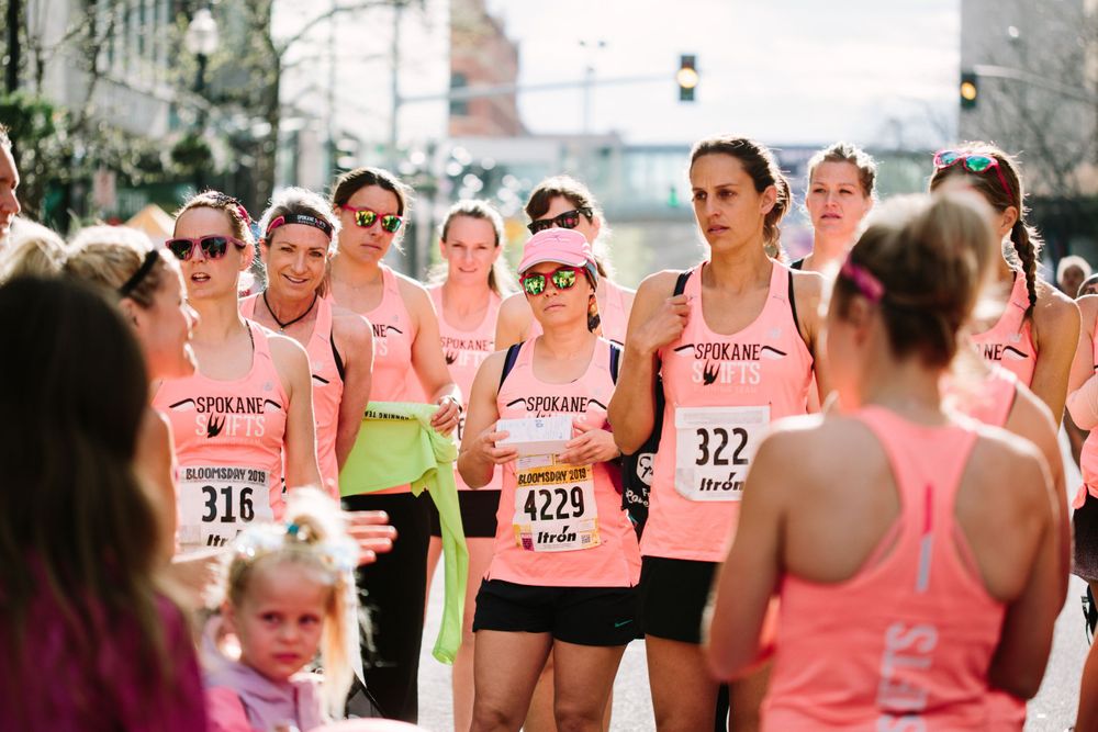 Group of women in matching pink tank tops gathered at outdoor running race event.
