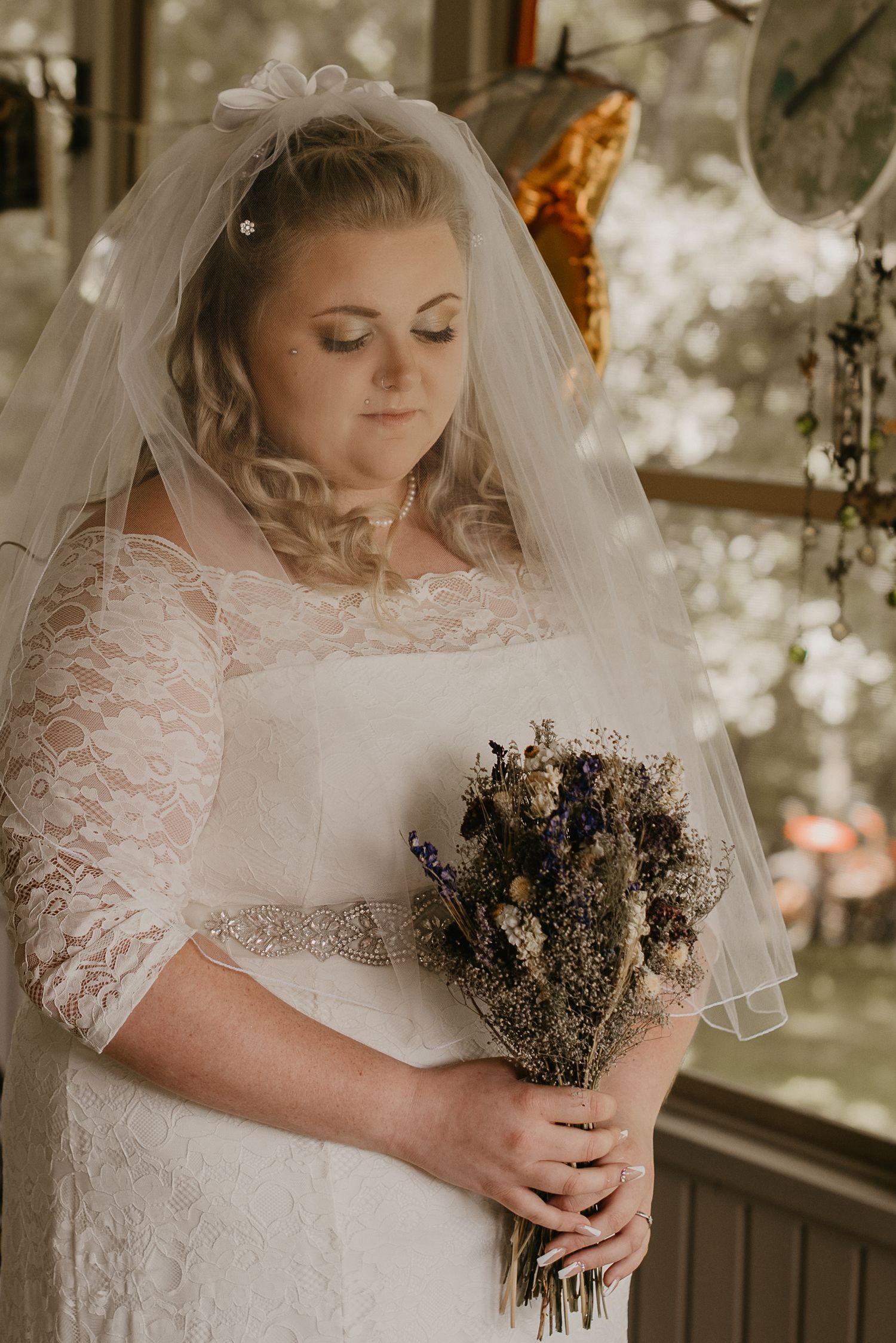 A bride in lace holding a dried flower bouquet poses for an elegant portrait.