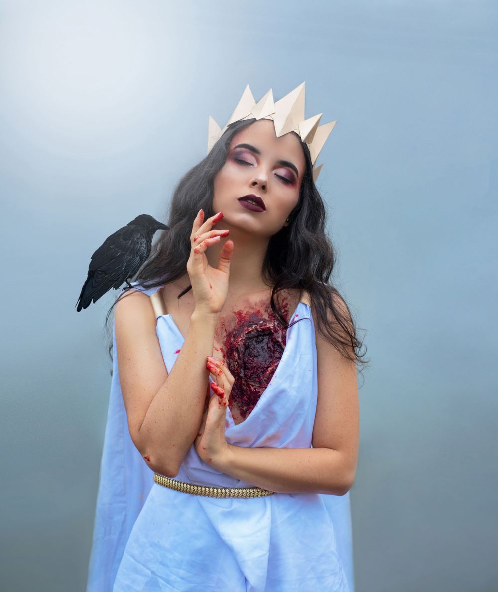 Dark fantasy portrait with crown, raven, and gothic styling against blue sky.