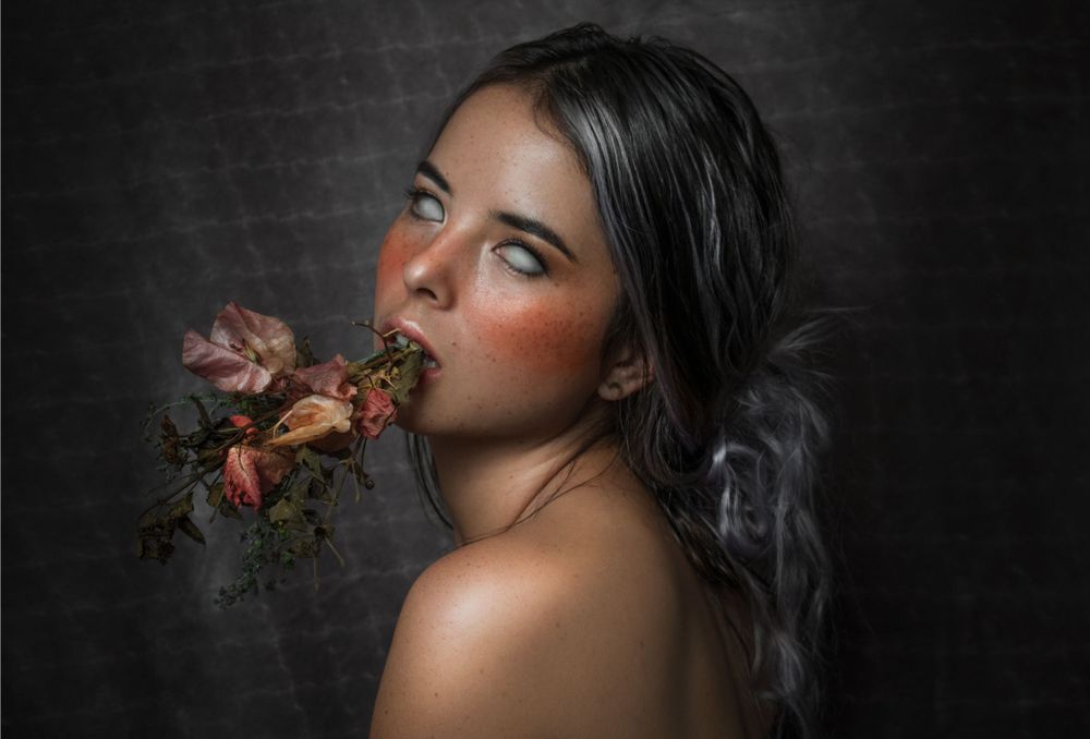 Artistic portrait featuring dark roses against a black background in moody lighting.