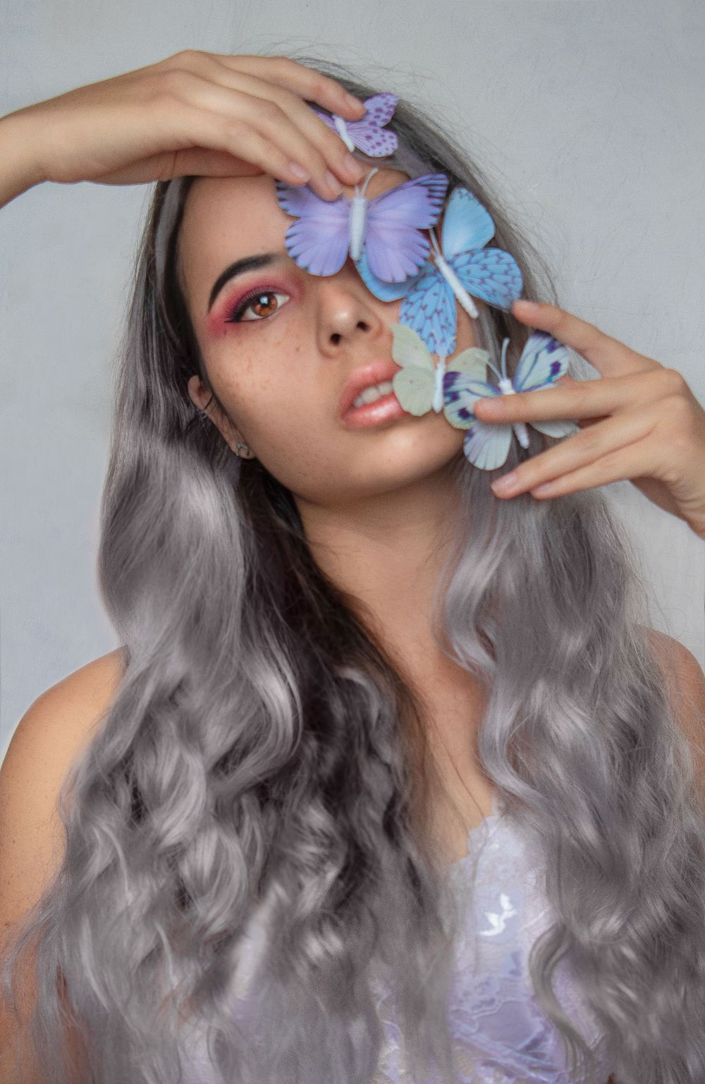 Dreamy portrait with purple and blue butterflies against gray background.