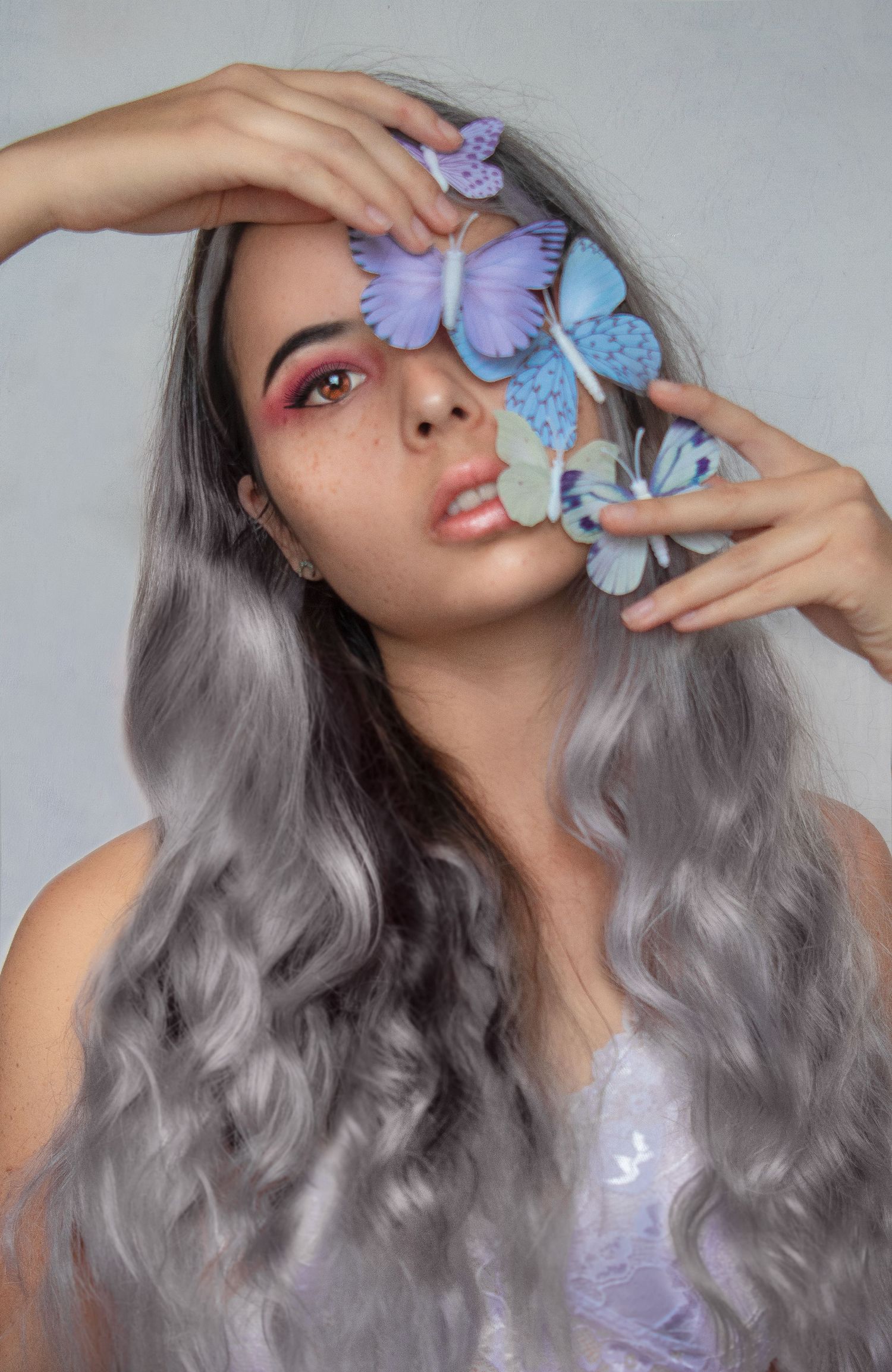 Dreamy portrait with purple and blue butterflies against gray background.