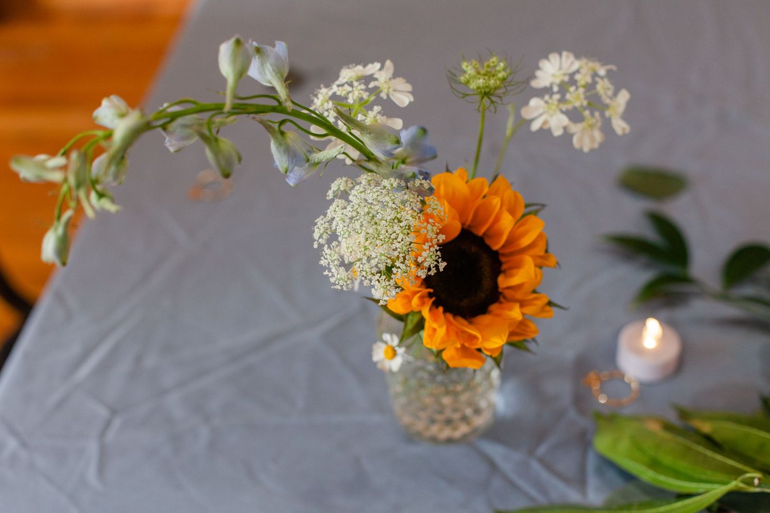 A simple floral centerpiece featuring a sunflower and white wildflowers in a glass vase.