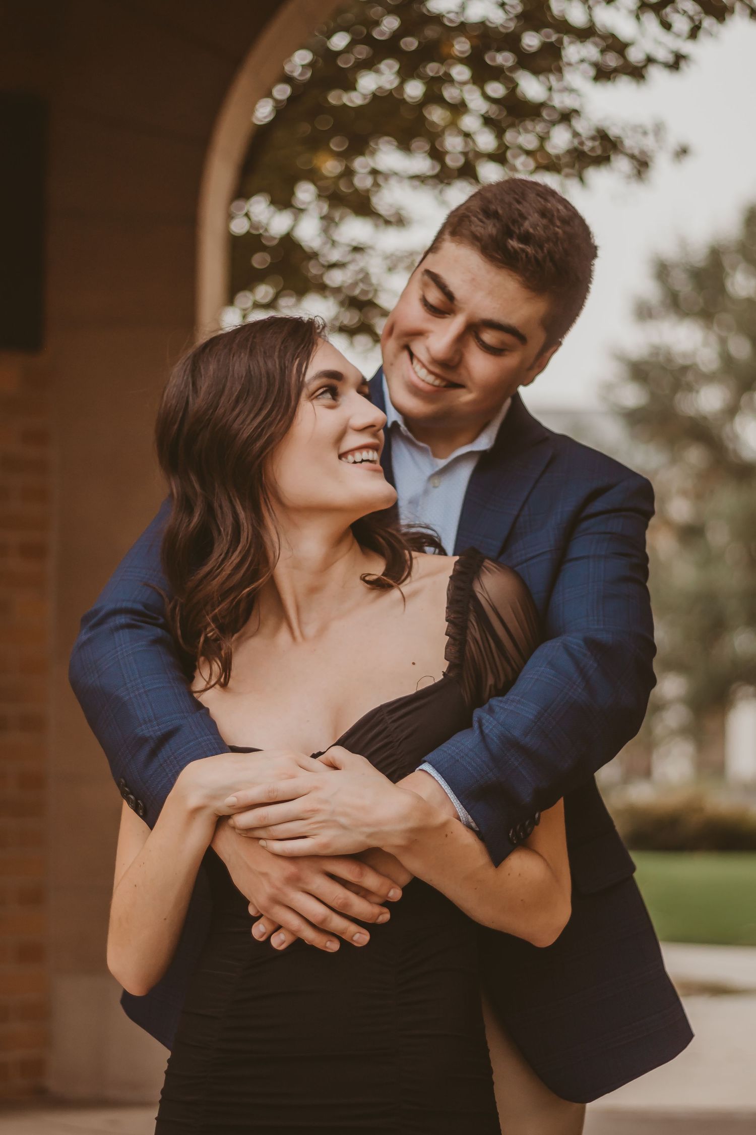 A romantic couple embracing, with the man in navy suit and woman in black dress.