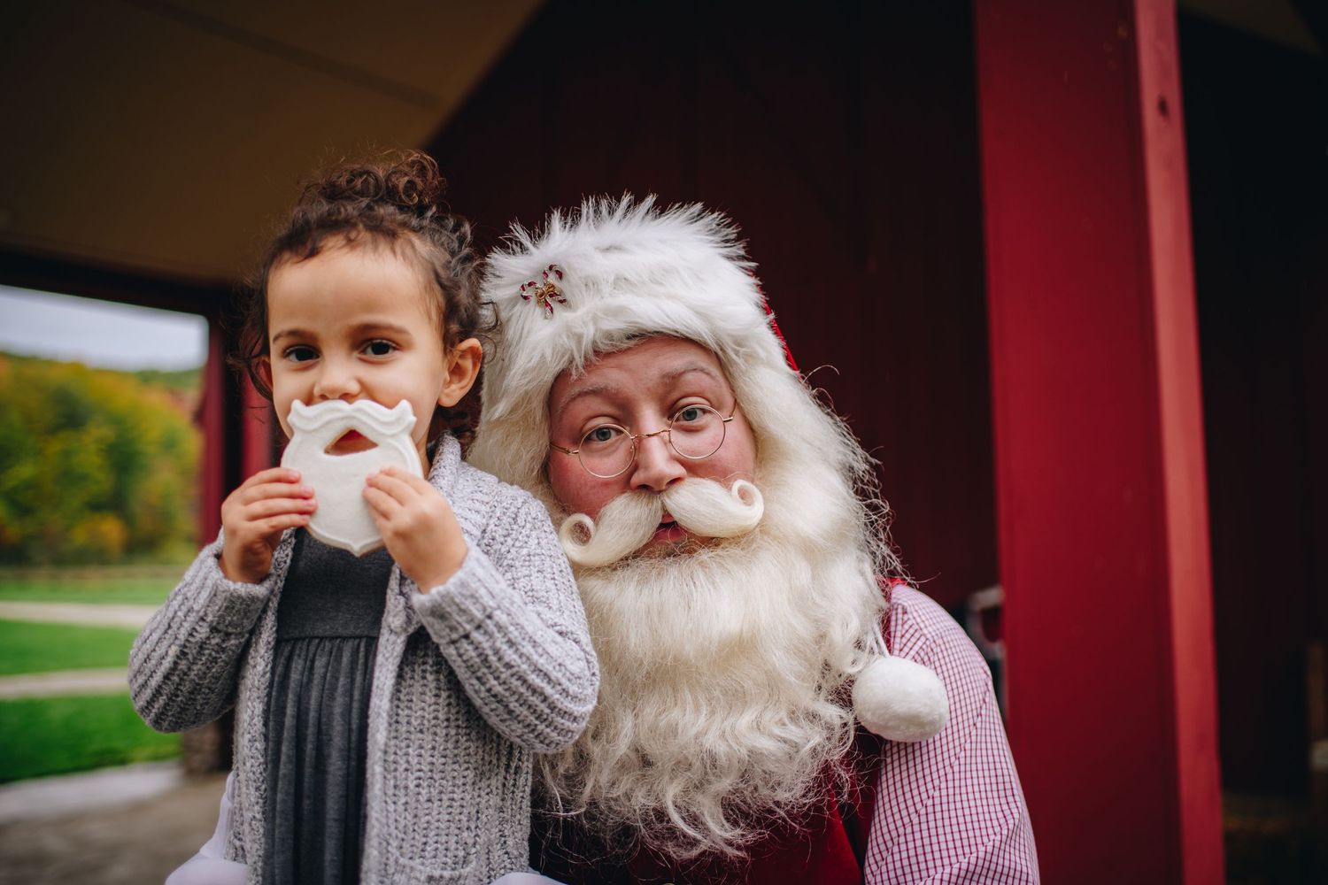little girl holds Santa beard cookie while Santa smiles behind her Kamms Corners