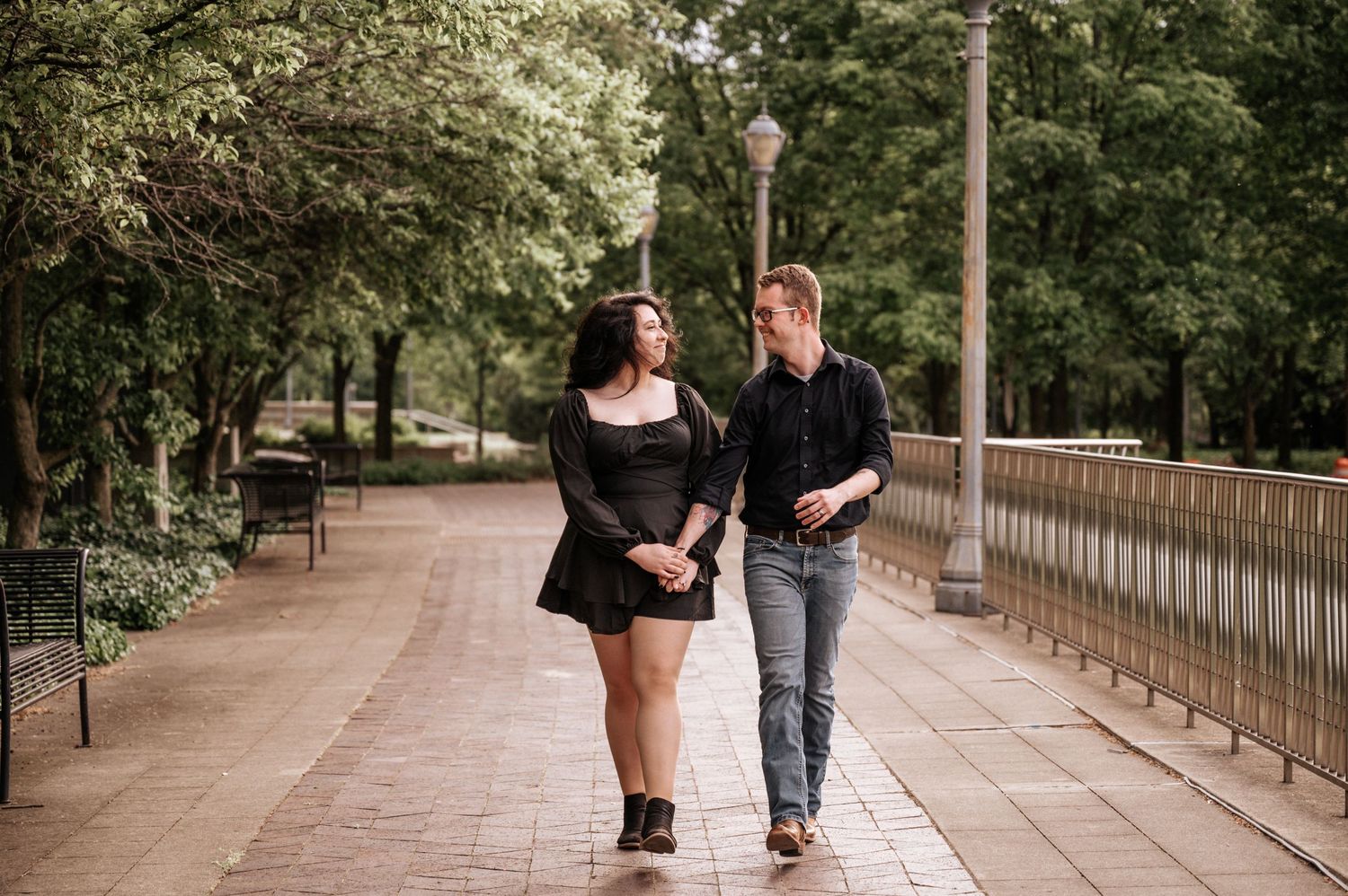 Couple walking together on tree-lined pathway in casual attire.
