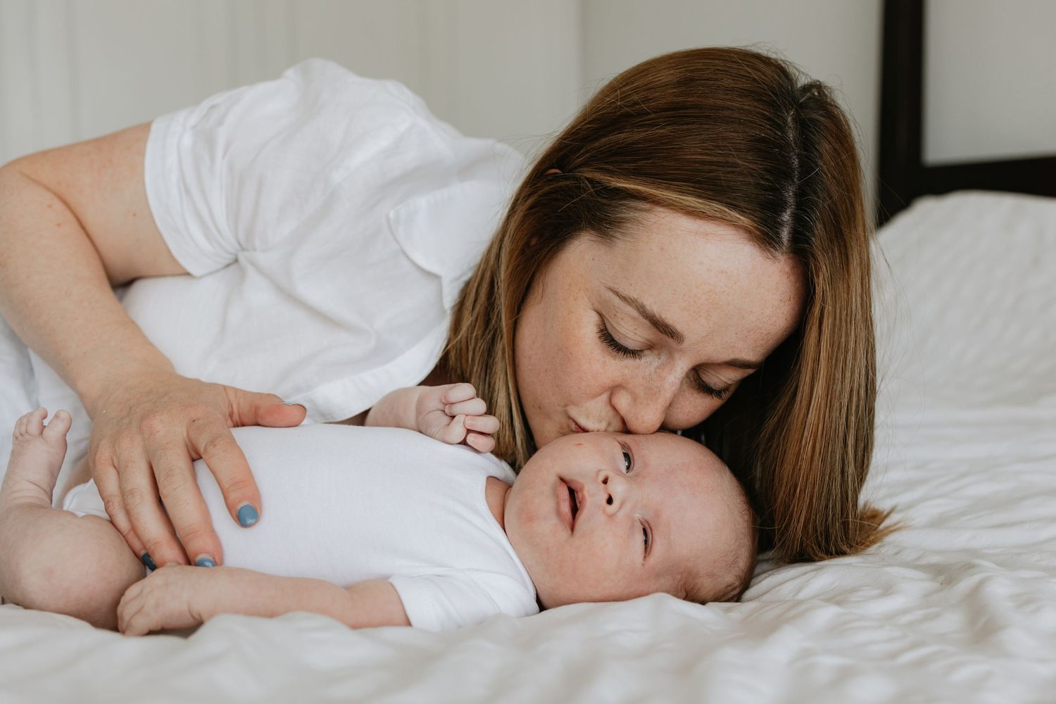 A tender moment between parent and baby lying on white bedding.