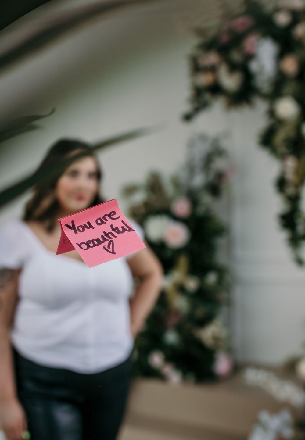 A stylish portrait with a pink sticky note reading 'You are beautiful' against floral backdrop.
