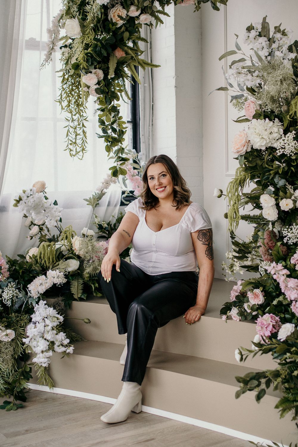 Portrait in a white room with lush floral arrangements and hanging greenery creating a romantic atmosphere.
